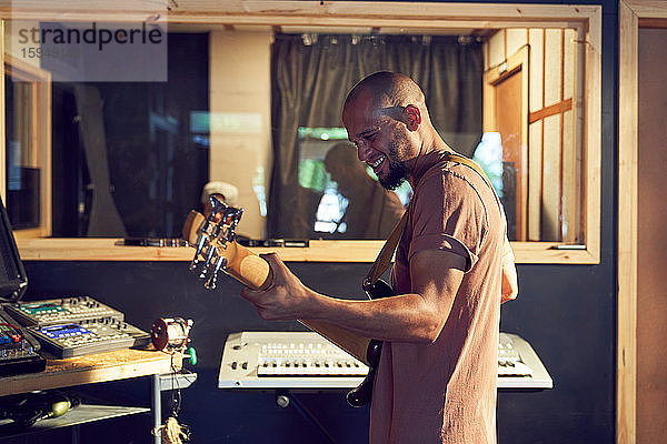 Glücklicher männlicher Musiker spielt Gitarre im Aufnahmestudio