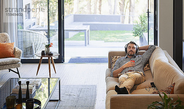 Mann entspannt sich auf dem Wohnzimmersofa  hört Musik mit Kopfhörern und mp3-Player