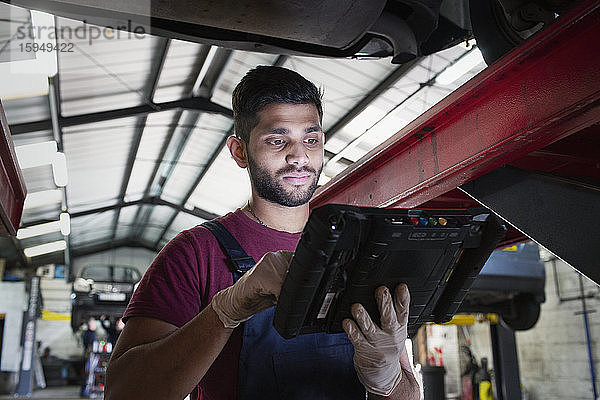 Fokussierter männlicher Mechaniker mit Diagnosegeräten in Autowerkstatt