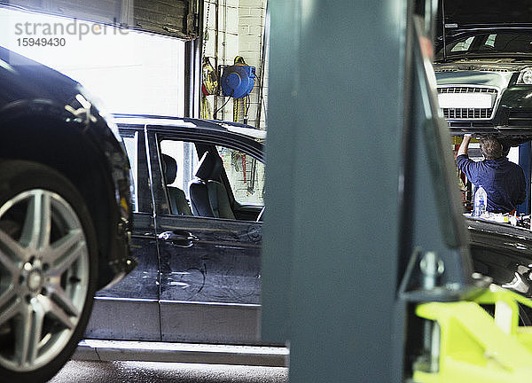 Männlicher Mechaniker  der unter dem Auto in einer Autowerkstatt arbeitet
