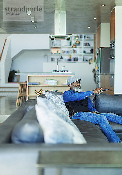 Mann mit Fernbedienung beim Fernsehen auf Wohnzimmersofa