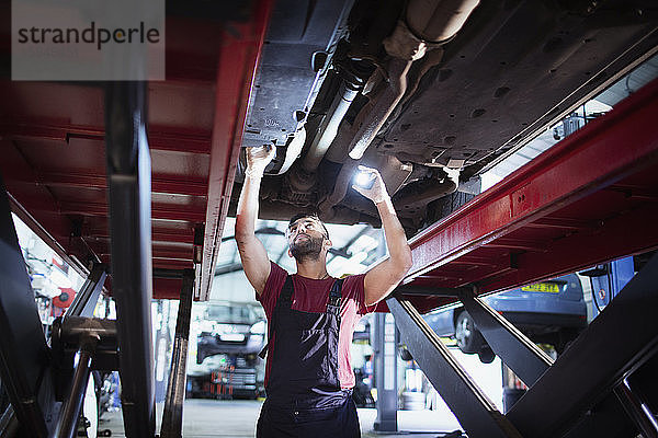 Männlicher Mechaniker mit Taschenlampe arbeitet unter dem Auto in einer Autowerkstatt