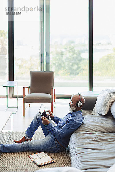 Mann mit Kopfhörern mit digitalem Tablett auf dem Wohnzimmerboden