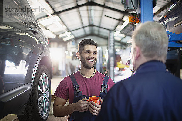 Lächelnde  fröhliche männliche Mechaniker  die sich unterhalten und Kaffee in der Autowerkstatt trinken