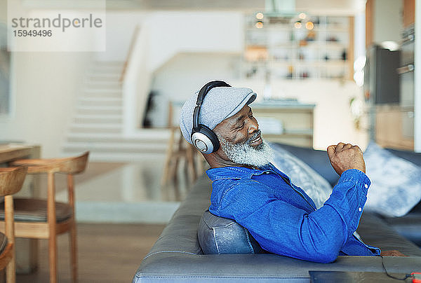 Glücklicher Mann mit Kopfhörern  der auf dem Wohnzimmersofa Musik hört