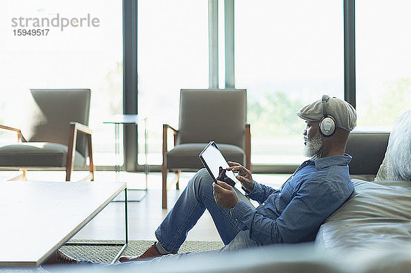 Mann entspannt sich  hört Musik mit Kopfhörern und digitalem Tablet im Wohnzimmer