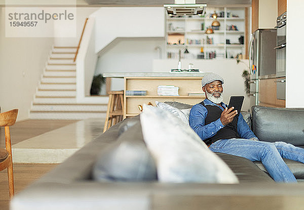 Mann benutzt digitales Tablett auf Wohnzimmer-Sofa