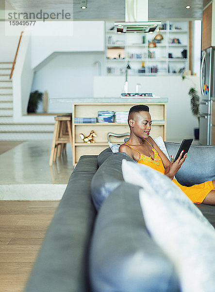 Junge Frau benutzt digitales Tablet auf Wohnzimmer-Sofa