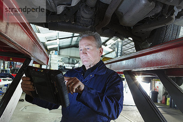 Männlicher Mechaniker benutzt Diagnosegerät unter Auto in Autowerkstatt