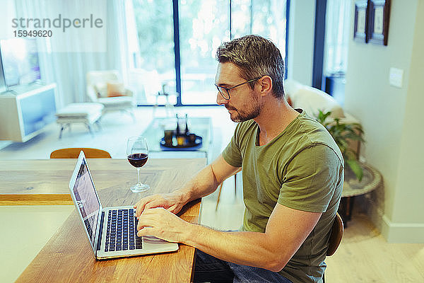 Mann arbeitet von zu Hause am Laptop  trinkt Rotwein in der Küche