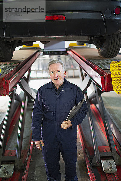 Porträt eines selbstbewussten Mechanikers unter einem Auto in einer Autowerkstatt