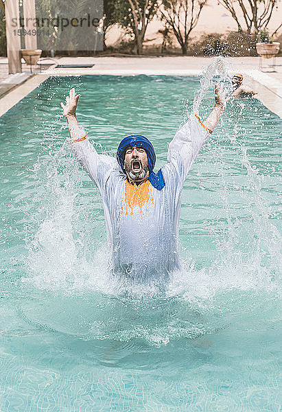 Mann mit blauem Turban spritzt Wasser in einem Schwimmbad