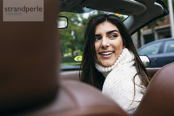 Lächelnde junge Frau schaut über die Schulter  während sie im Auto unterwegs ist
