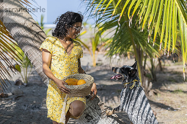 Junge Frau hält mit ihrem Hund einen Obstkorb am Strand  Costa Rica