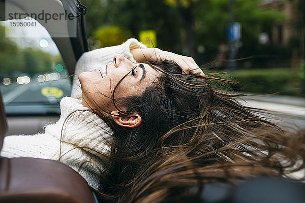 Glückliche Frau mit zerzaustem Haar genießt Wind im Cabrio