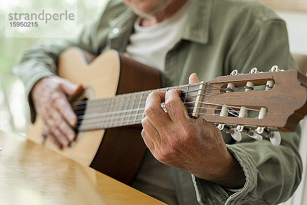 Ein Teil eines Rentners im Ruhestand  der zu Hause sitzend Gitarre übt