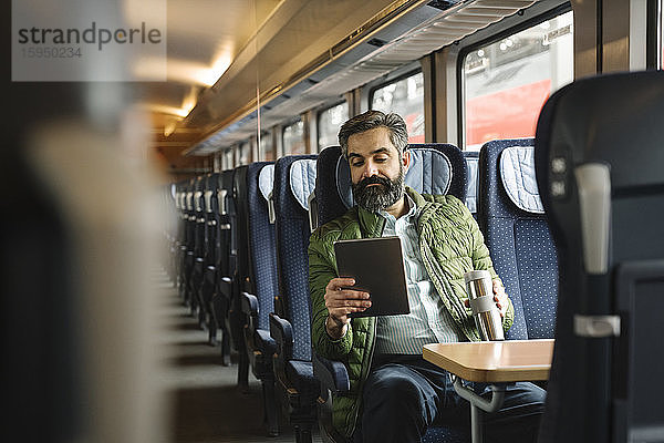 Mann sitzt mit Tablette im Zug