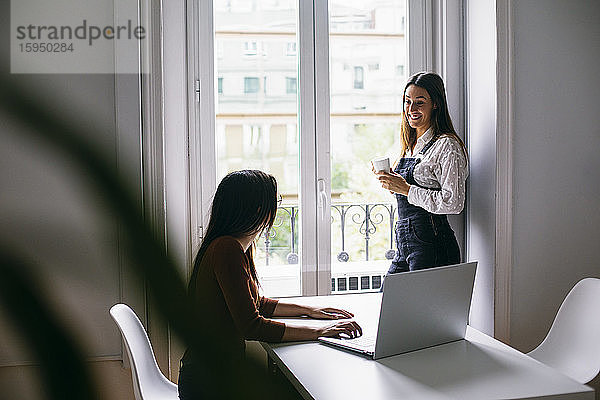Geschäftsfrau trinkt Kaffee  während ein Kollege im Büro am Laptop arbeitet