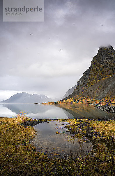 Island  Wolken über ruhigem Seeufer mit Bergen im Hintergrund