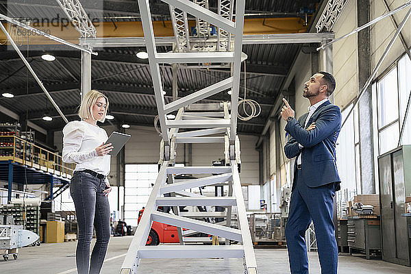 Geschäftsmann und junge Frau mit Tablette im Gespräch in einer Fabrik
