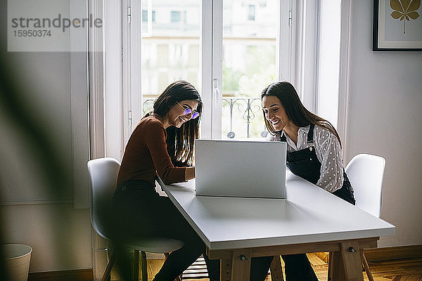 Lächelnde Kollegen diskutieren über Laptop am Schreibtisch im Büro