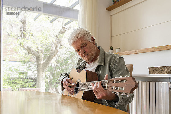 Älterer Mann zupft Gitarrensaiten beim Üben zu Hause
