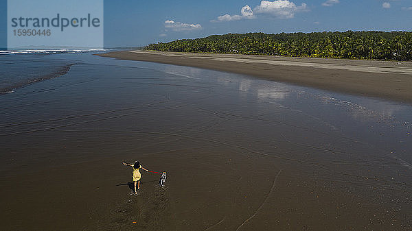Unbeschwerte junge Frau geht mit ihrem Hund am Strand spazieren  Costa Rica