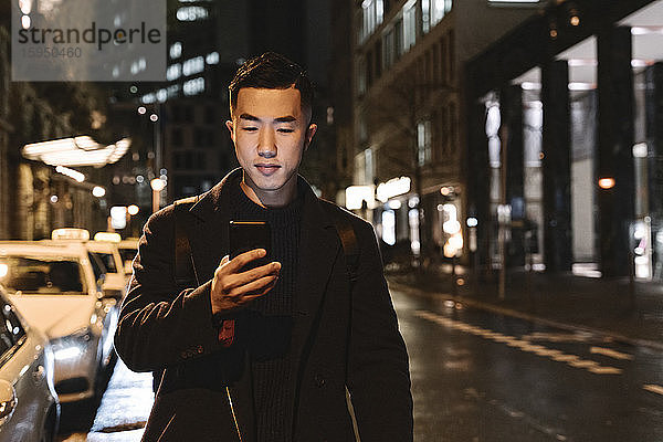 Mann benutzt Smartphone beim nächtlichen Spaziergang in der Stadt
