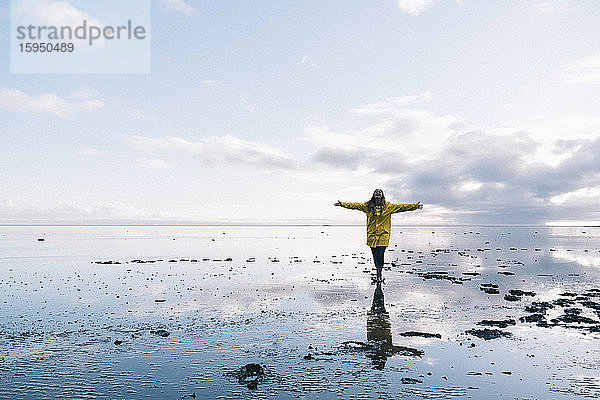 Frau mit ausgestreckten Armen  die sich im Meer am Strand des Naturreservats Hvalnes  Island  spiegeln