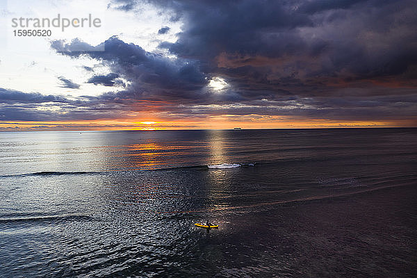 Mauritius  Hubschrauberansicht dunkler Gewitterwolken über einem einsamen Surfer beim Paddelboarden im Indischen Ozean bei Sonnenuntergang