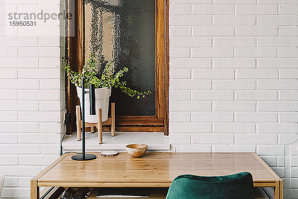Holztisch und -stuhl gegen Zimmerpflanze auf der Fensterbank im Heimbüro
