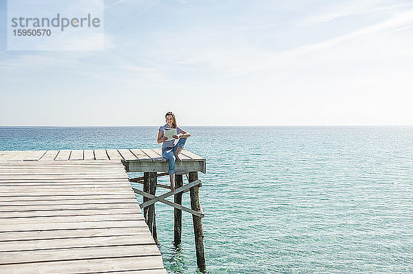 Frau sitzt am Steg und liest Zeitschrift  Mallorca  Spanien