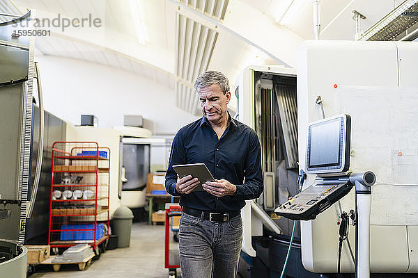 Reifer Mann arbeitet in der Produktionshalle einer Fabrik mit einem digitalen Tablett