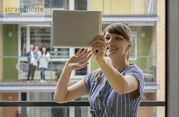 Porträt einer lächelnden jungen Frau  die ein digitales Tablet für Video-Chat mit ihren Nachbarn benutzt