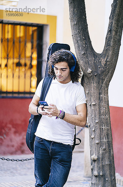 Junger Mann benutzt Mobiltelefon beim Tragen einer Gitarrentasche  Santa Cruz  Sevilla  Spanien