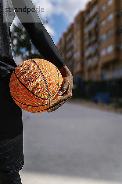 Junger Mann hält Basketball auf Basketballfeld