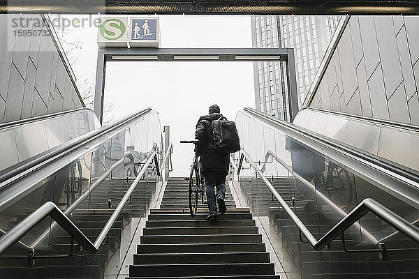 Geschäftsmann mit Fahrrad auf der Treppe beim Verlassen der U-Bahn-Station in der Stadt