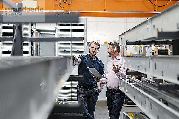 Zwei Männer diskutieren in einer Fabrik über einen Plan
