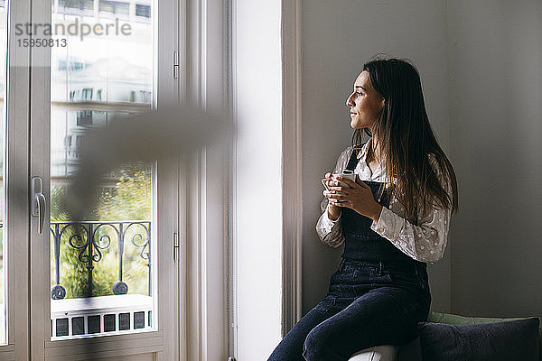 Nachdenkliche Geschäftsfrau schaut durchs Fenster  während sie im Büro Kaffee trinkt