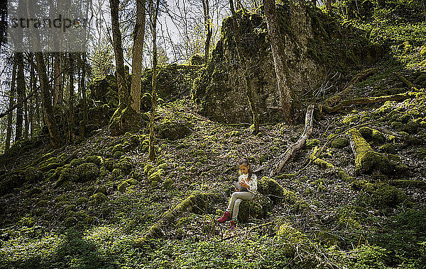 Mädchen sitzt im Wald der Schwäbischen Alb und benutzt während des Wanderwochenendes ein digitales Tablet