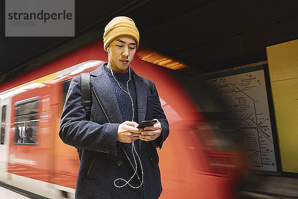 Eleganter Mann mit Smartphone und Kopfhörern in der U-Bahn-Station