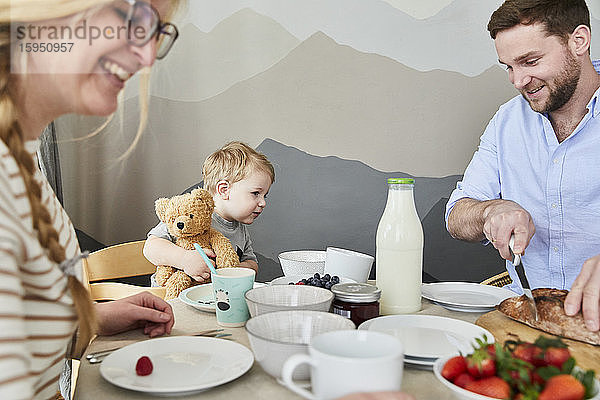Kleiner Junge sitzt am Frühstückstisch und sieht seinem Vater beim Brotschneiden zu