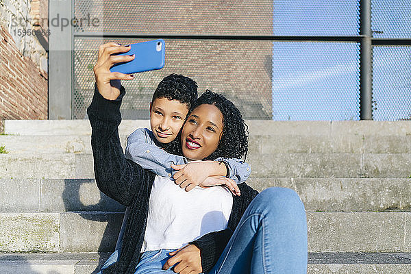 Mutter und Sohn sitzen gemeinsam auf Stufen  die sich mit dem Smartphone selbstständig machen