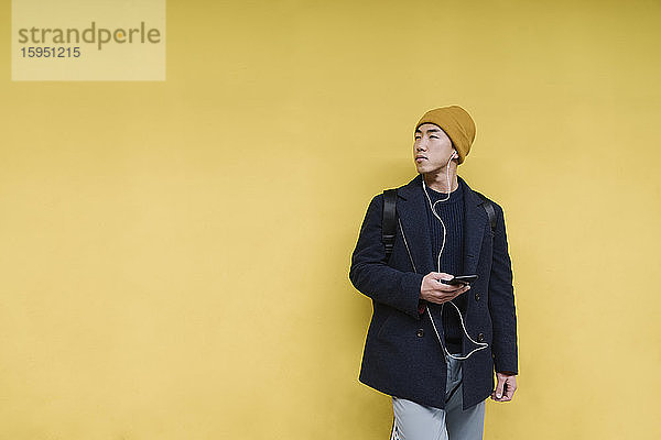 Eleganter Mann mit gelbem Hut und Kopfhörer mit Smartphone