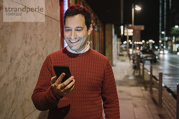 Porträt eines glücklichen Unternehmers in der Stadt beim Blick aufs Handy  Frankfurt  Deutschland
