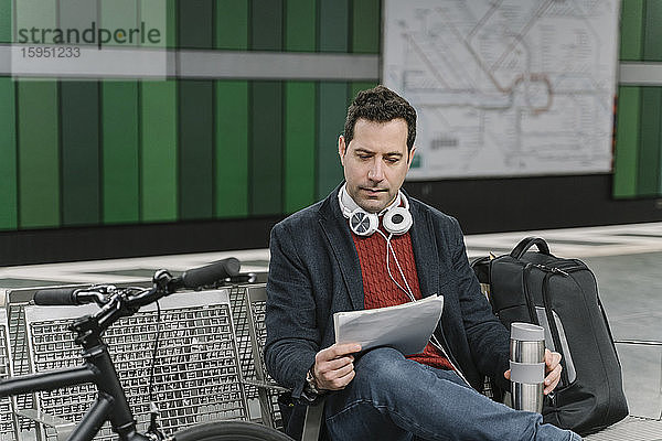 Geschäftsmann mit Fahrrad liest Dokumente  während er am Bahnsteig einer U-Bahn-Station sitzt  Frankfurt  Deutschland