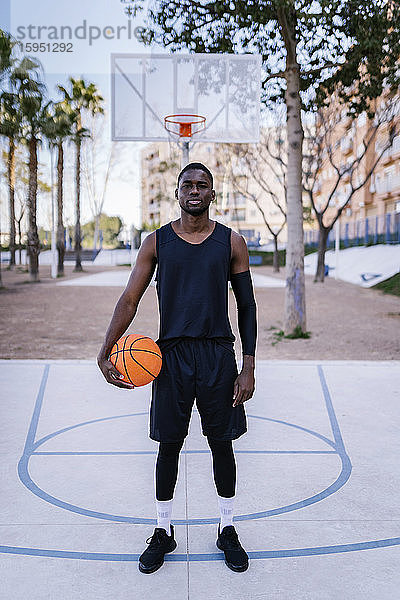 Junger Mann hält Basketball auf Basketballfeld