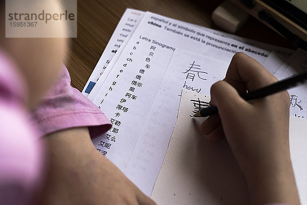 Beschnittenes Bild eines Mädchens  das am Schreibtisch chinesischen Text auf Papier schreibt