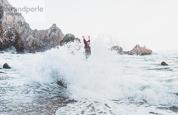 Junge Frau  die mit einer großen Welle auf einem Felsen steht  Praia da Ursa  Lissabon  Portugal