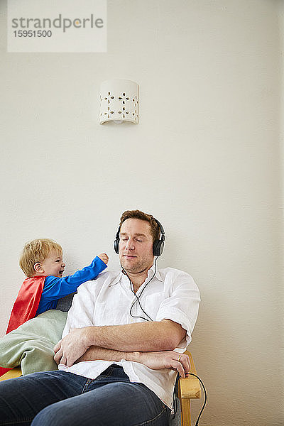 Junge im Superman-Kostüm und nervender Vater beim Musikhören mit Kopfhörern